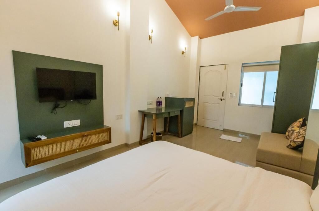 A hotel room with a bed, a desk, a TV mounted on the wall, a ceiling fan, and a window.