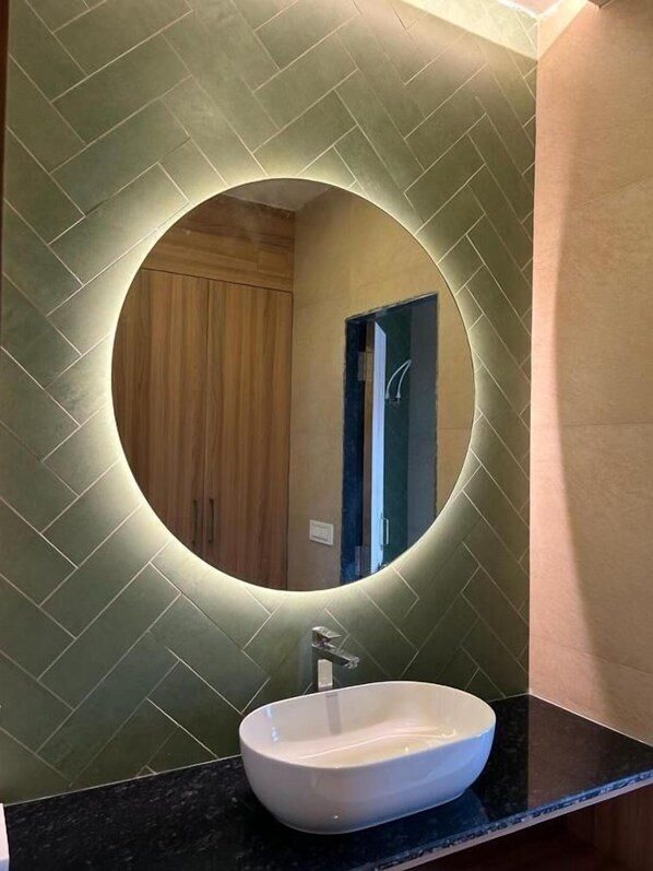 Un baño con un espejo redondo, un lavamanos blanco y una pared con motivo de espinilla.