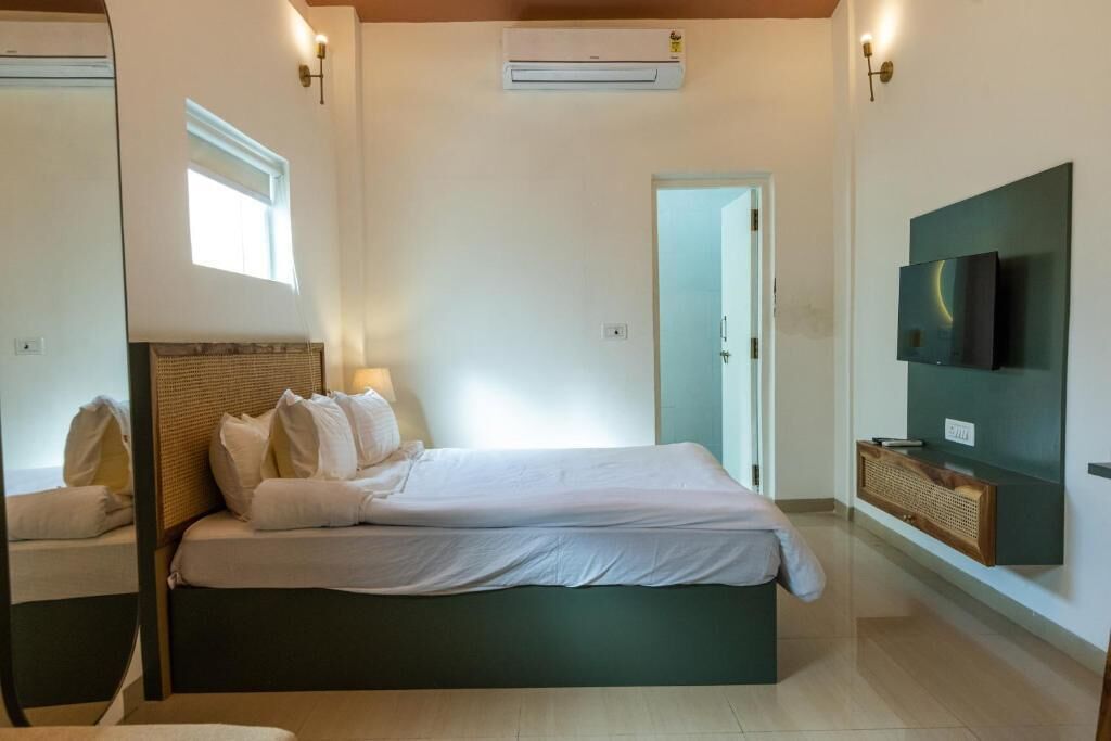 A bedroom with a bed, bedside lamps, a TV mounted on the wall, and an air conditioning unit.
