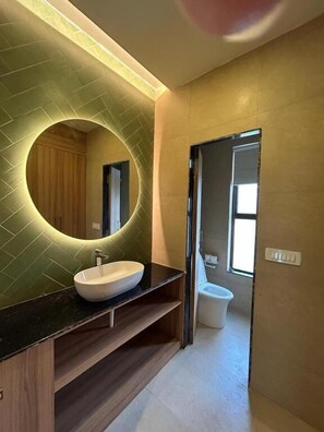 Een moderne badkamer met een ronde spiegel, een witte wastafel en een toilet.