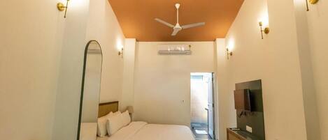 Un dormitorio con cama, ventilador de techo, televisor y un espejo grande.