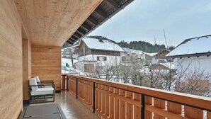 A wooden balcony with a metal railing, a sofa, and a view of snow-covered buildings in the background. - New & high-quality furnished guest house in a quiet location - Burgberg im Allgäu (Burgberg im Allgäu)
