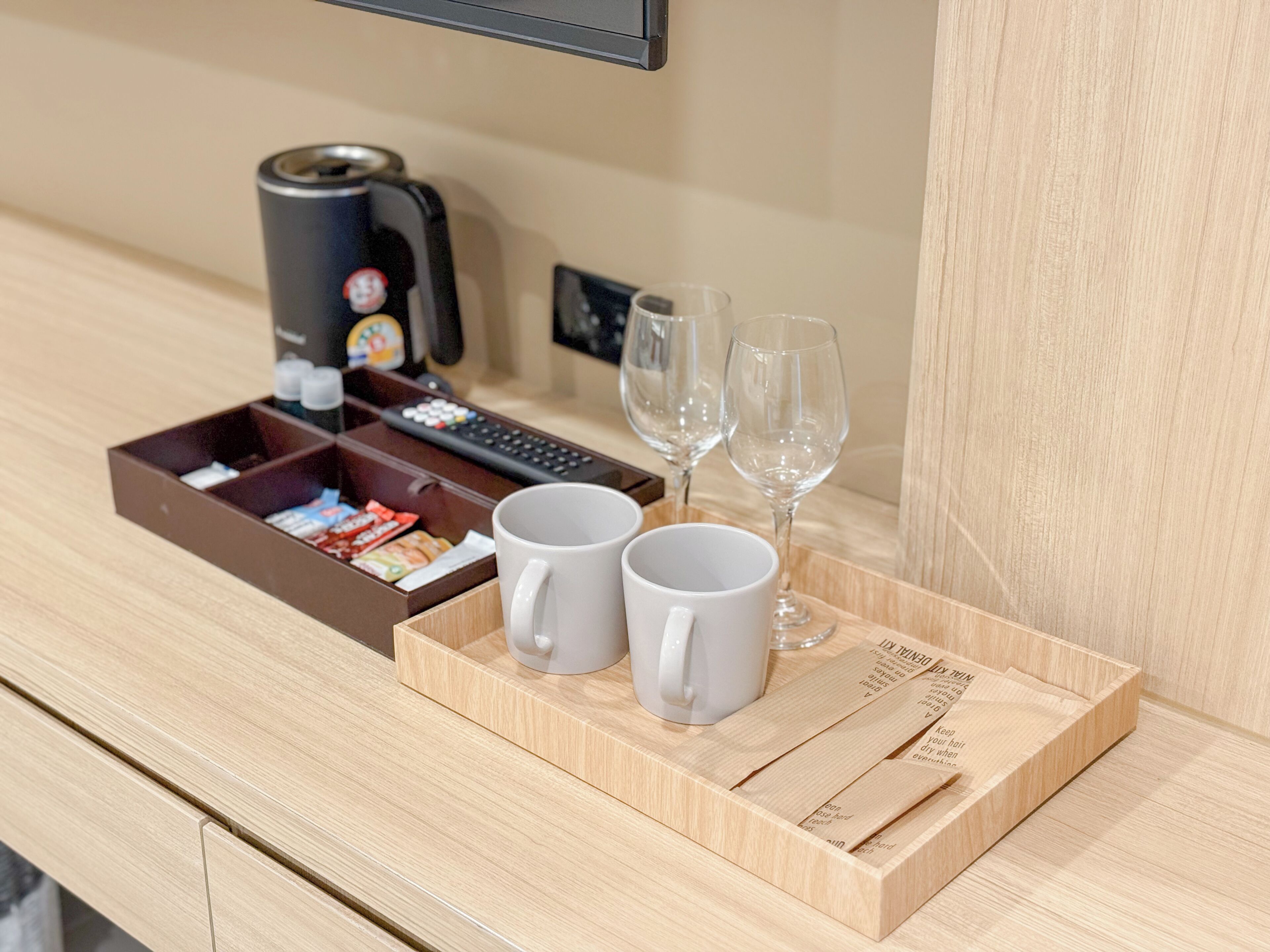 Ein Holztablett mit zwei weißen Tassen, einer Fernbedienung und einer Kaffeemaschine auf einer Hotelarbeitsfläche.