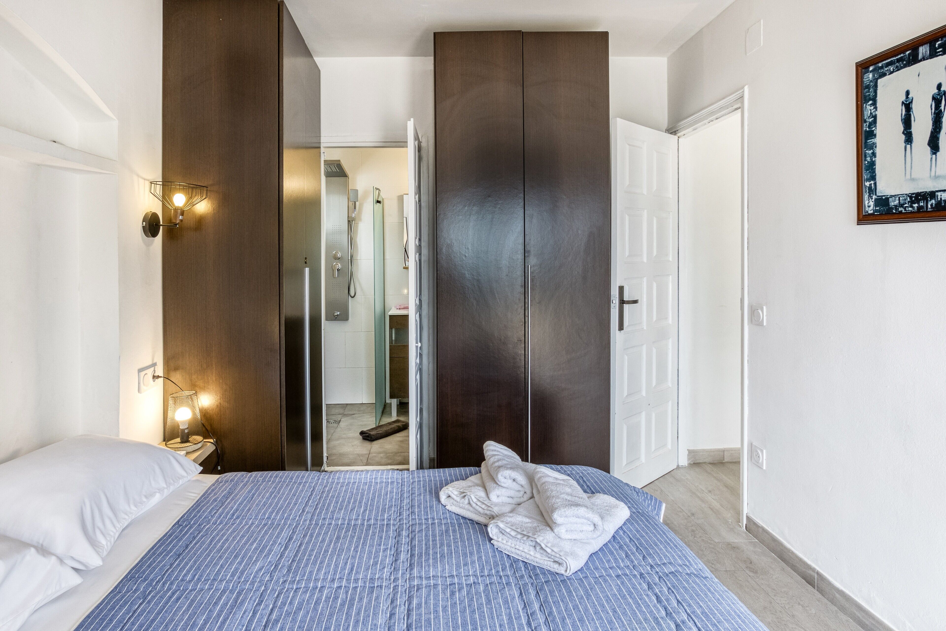 Un dormitorio con una cama, un armario, una mesita de noche y un aplique de pared.