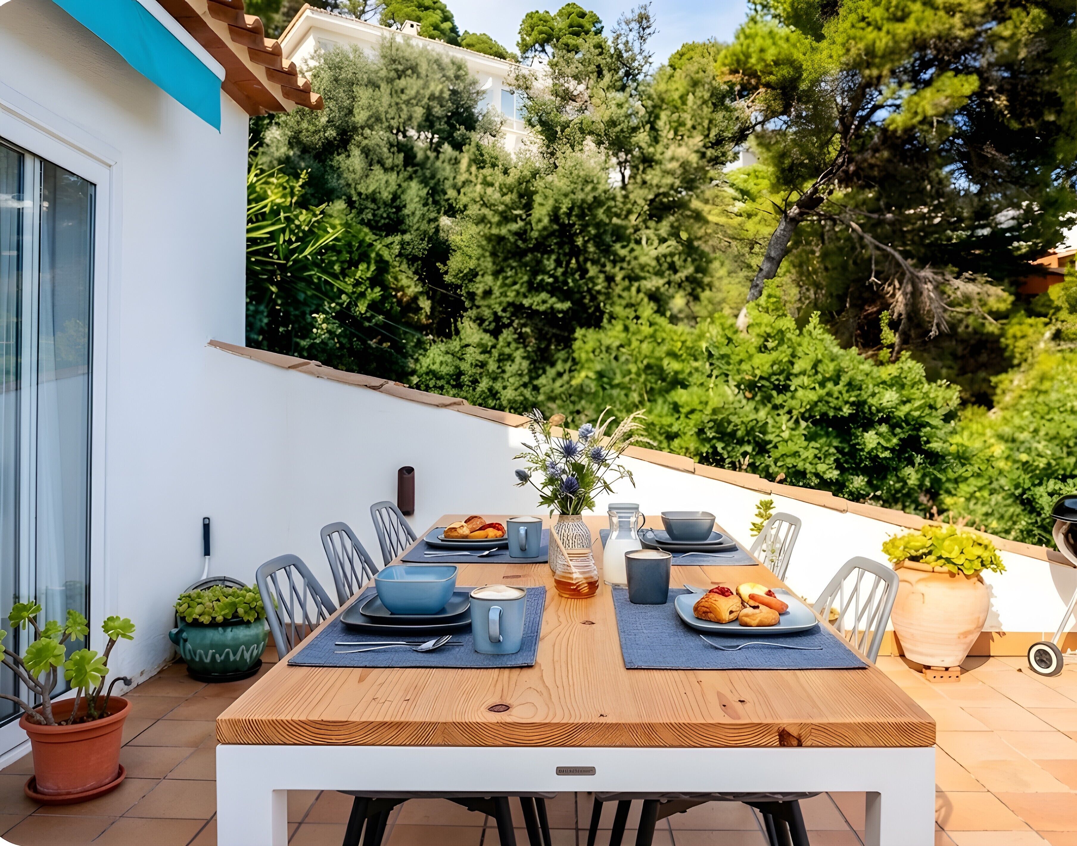 Uma área de refeições ao ar livre com mesa de madeira, cadeiras e diversos pratos e bebidas.