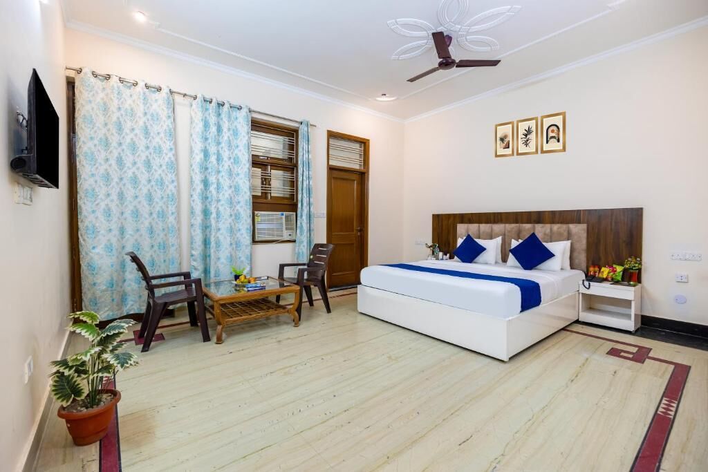 A bedroom with a bed, a ceiling fan, a TV, a window with curtains, and a small table with chairs.