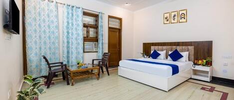 A bedroom with a bed, a ceiling fan, a TV, a window with curtains, and a small table with chairs.
