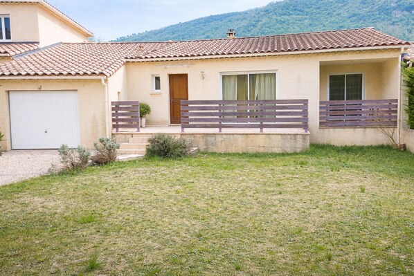 A single-story house with a tiled roof, a front door, a small porch with a bench, and a grassy yard. - Escape to the Cévennes: house at the foot of Mont Cévenol, near Ardèche (Bessèges)