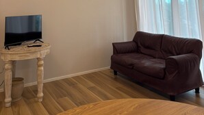 A living room with a brown leather sofa, a television on a wooden table, and a window with sheer curtains. - Apartment in the center of Igea Marina (Bellaria-Igea Marina)