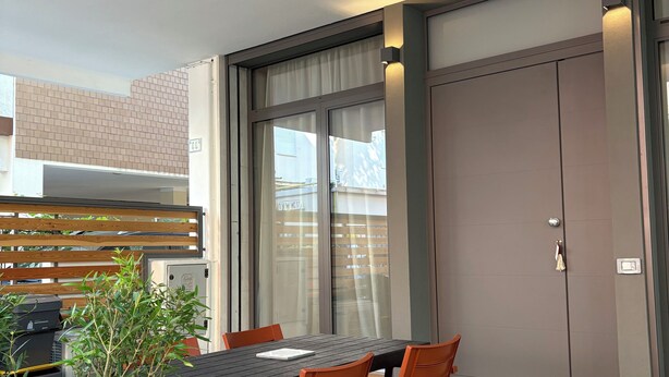 An outdoor dining area with a table and chairs, a potted plant, and a sliding glass door leading to a balcony. - Apartment in the center of Igea Marina (Bellaria-Igea Marina)