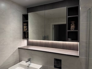 Casa de banho moderna com um espelho grande, lavatório e prateleira com objetos decorativos.