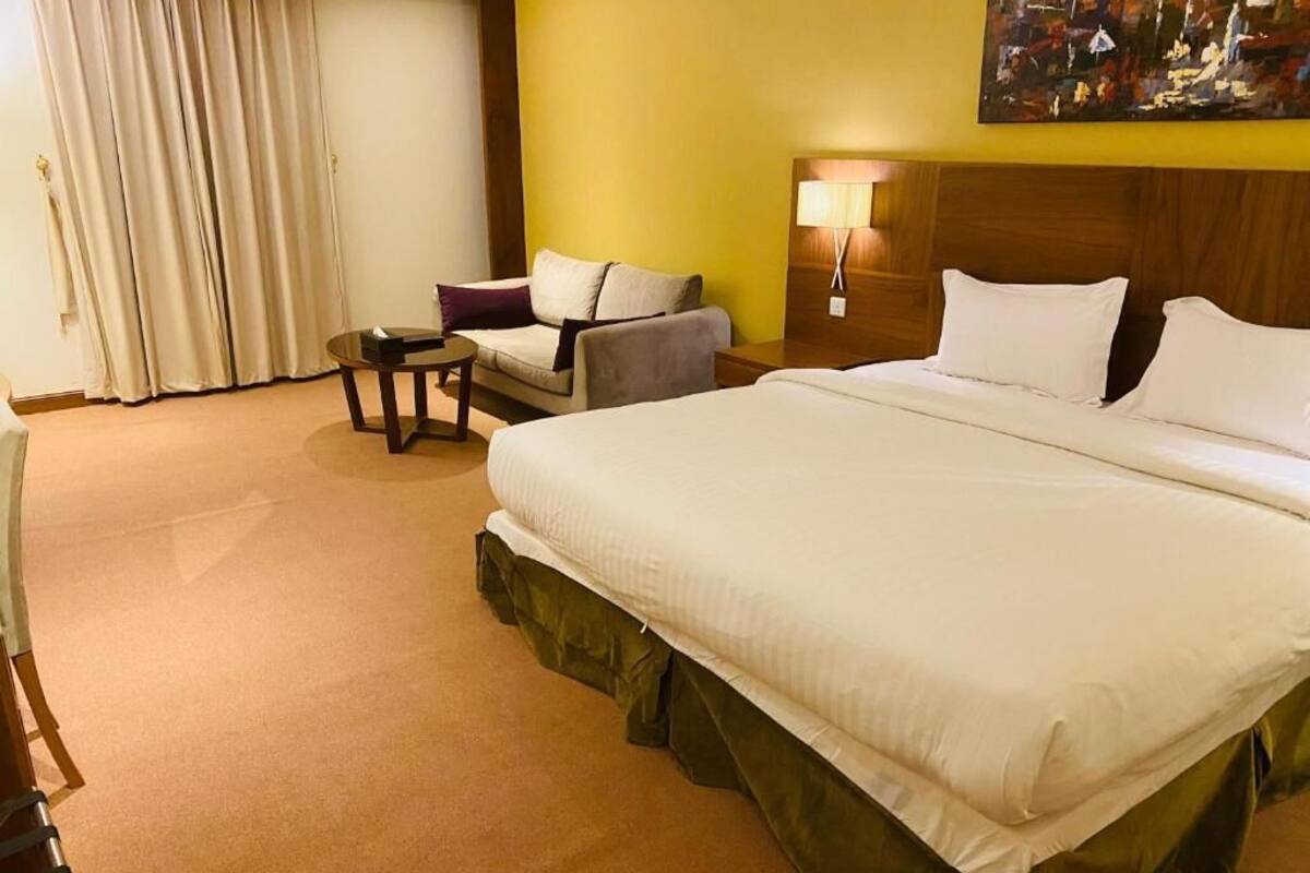 Una habitación de hotel con una cama grande, un sofá, una mesita y una lámpara.