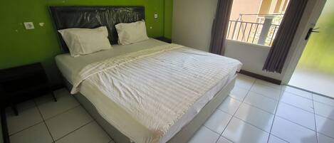 Una cama bien hecha en una habitación con paredes verdes, un cabecero negro y una ventana con vistas al exterior.
