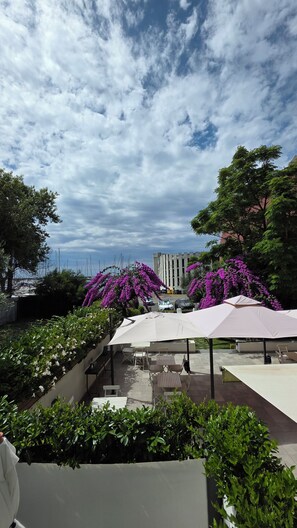 An outdoor seating area with umbrellas, surrounded by lush greenery and purple flowering plants. - BLU HOTEL (Lavagna)