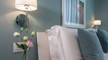 Habitación de hotel con una cama, ropa de cama blanca, una mesita de vidrio con un florero y lámparas de pared.