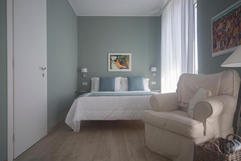 A bedroom with a bed, a chair, a painting, and a lamp.