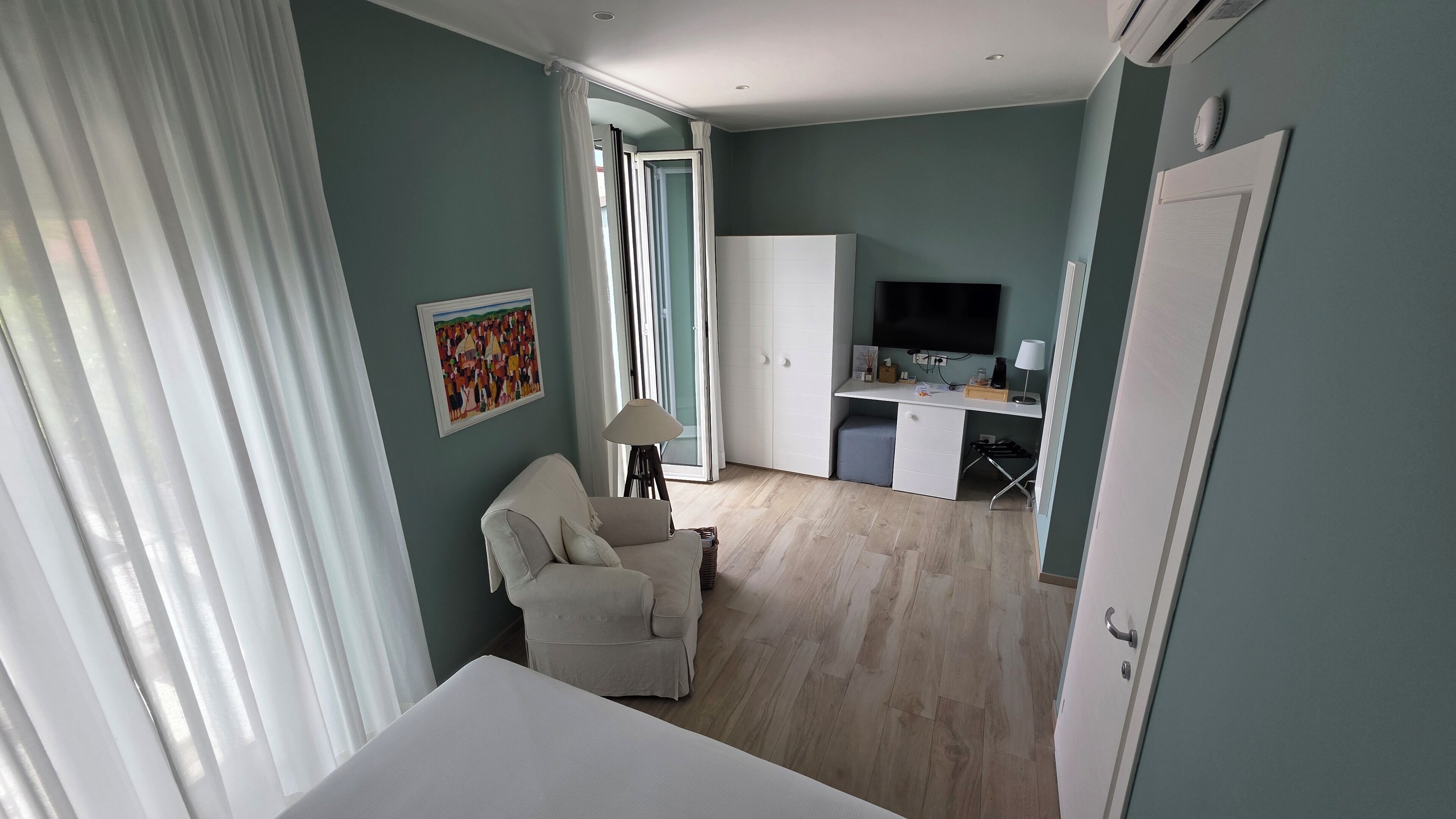 Quarto com cama, escrivaninha com televisão, cadeira e quadro na parede.