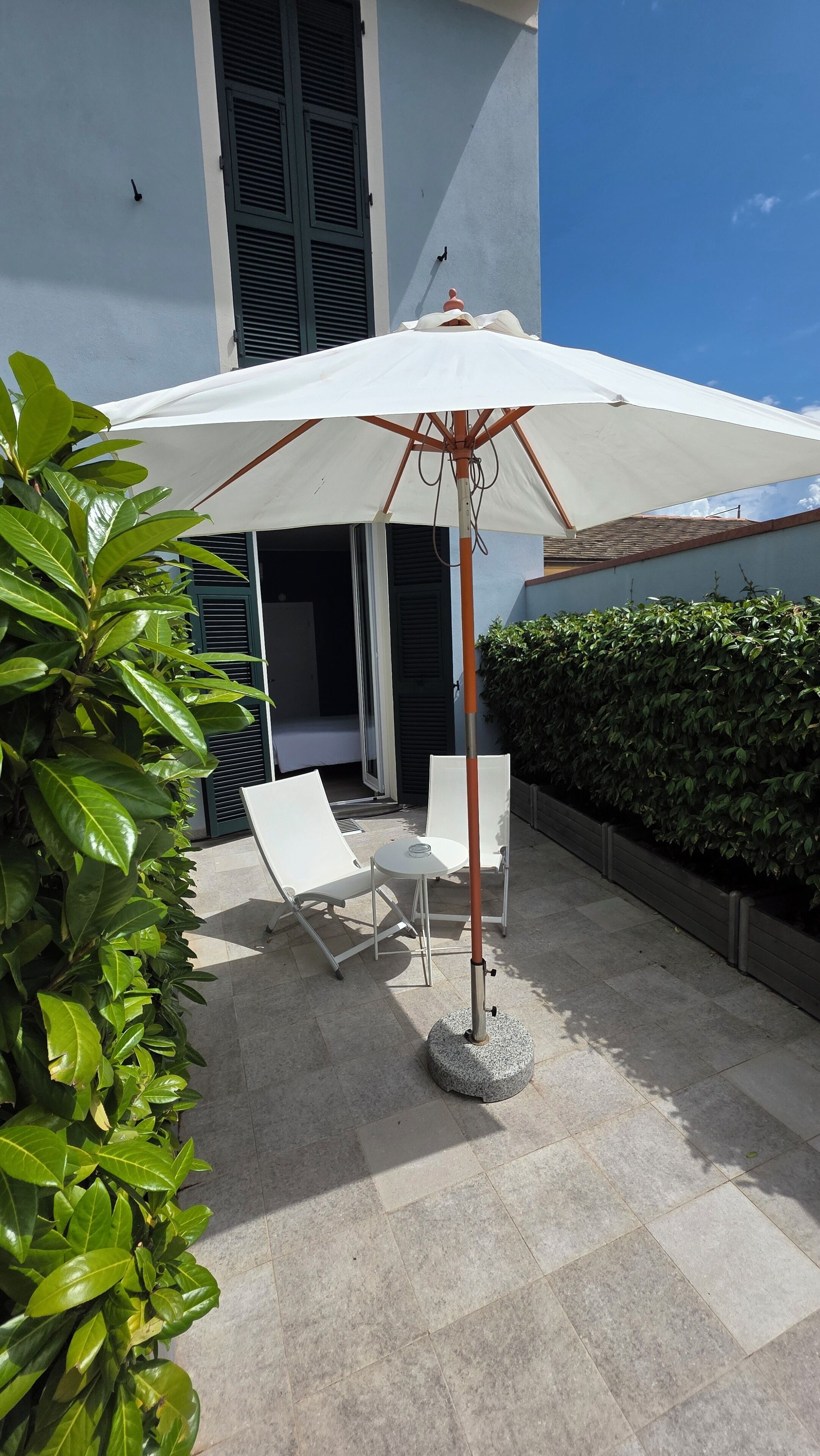 Un patio con una sombrilla blanca, dos sillas blancas y una planta en maceta.