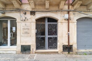 Eine Gebäudefassade mit einem großen Bogenfenster, einer Tür mit aufwendiger Metallverzierung und einem Schild, das eine Bibliothek anzeigt.