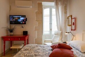 Ein Schlafzimmer mit einem Bett, einem Schreibtisch, einem Stuhl, einem Fernseher und einem Fenster mit Vorhängen.