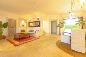 A spacious living room with a sofa, a patterned ottoman, and a dining area with a table and chairs. - Nuru Villa (Watamu)