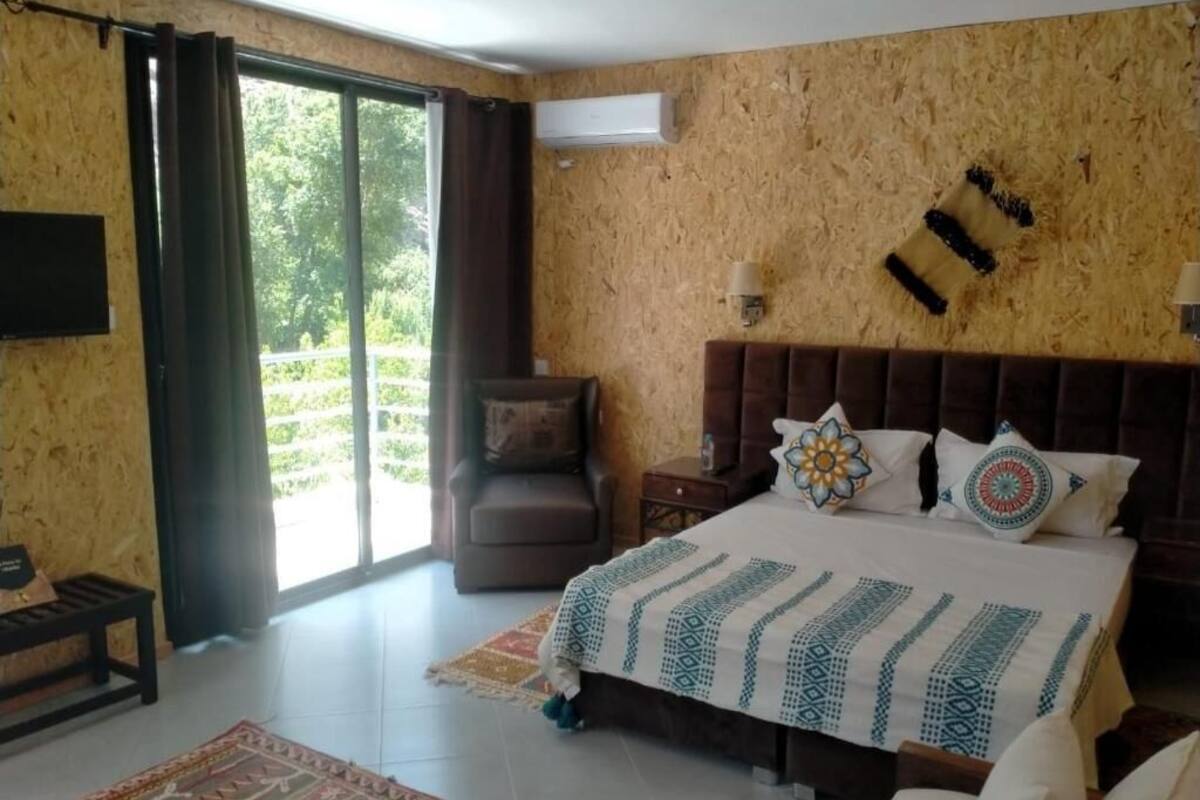 Une chambre avec un grand lit, un canapé, une télévision et une porte-fenêtre coulissante donnant sur un balcon.