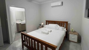 A bedroom with a wooden bed, a bedside table, an air conditioning unit, and a ceiling fan.