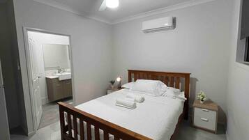 Quarto com cama de madeira, mesa de cabeceira, aparelho de ar condicionado e ventoinha de teto.