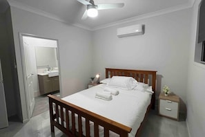 A bedroom with a wooden bed, a bedside table, an air conditioning unit, and a ceiling fan. - 2 House Together 7 BR Ideal for Large Families (Hillcrest)