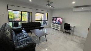 A modern living room with a black leather sofa, a small coffee table, a TV on a white stand, and a ceiling fan.