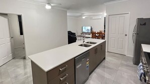 A modern kitchen with a central island, built-in dishwasher, and a dining area with a TV.