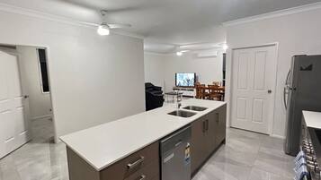Cozinha moderna com ilha central, máquina de lavar louça embutida e área de jantar com televisão.