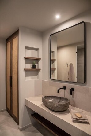 A modern bathroom with a large mirror, a stone basin, wooden shelves, and a towel rack. - Aku Suites with private pools (Malia)