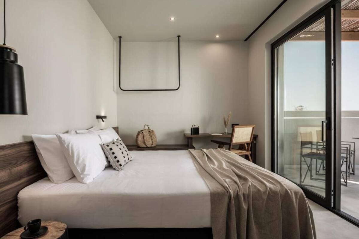 A modern hotel room with a large bed, a desk, and a balcony with outdoor seating.