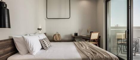 A modern hotel room with a large bed, a desk, and a balcony with outdoor seating.
