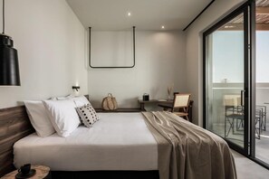 A modern hotel room with a large bed, a desk, and a balcony with outdoor seating. - Aku Suites with private pools (Malia)