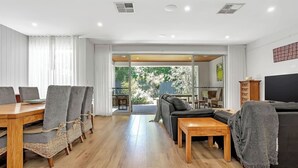 Una sala de estar moderna con suelo de madera, un sofá, un televisor y un comedor con sillas y una mesa.