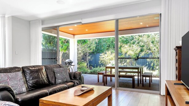 Una sala de estar moderna con un sofá de cuero, una mesa de centro de madera y una puerta de cristal que da a un patio con mobiliario exterior.