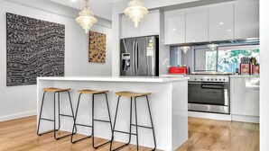 Una cocina moderna con una isla central, taburetes de bar, electrodomésticos de acero inoxidable y obras de arte en las paredes.