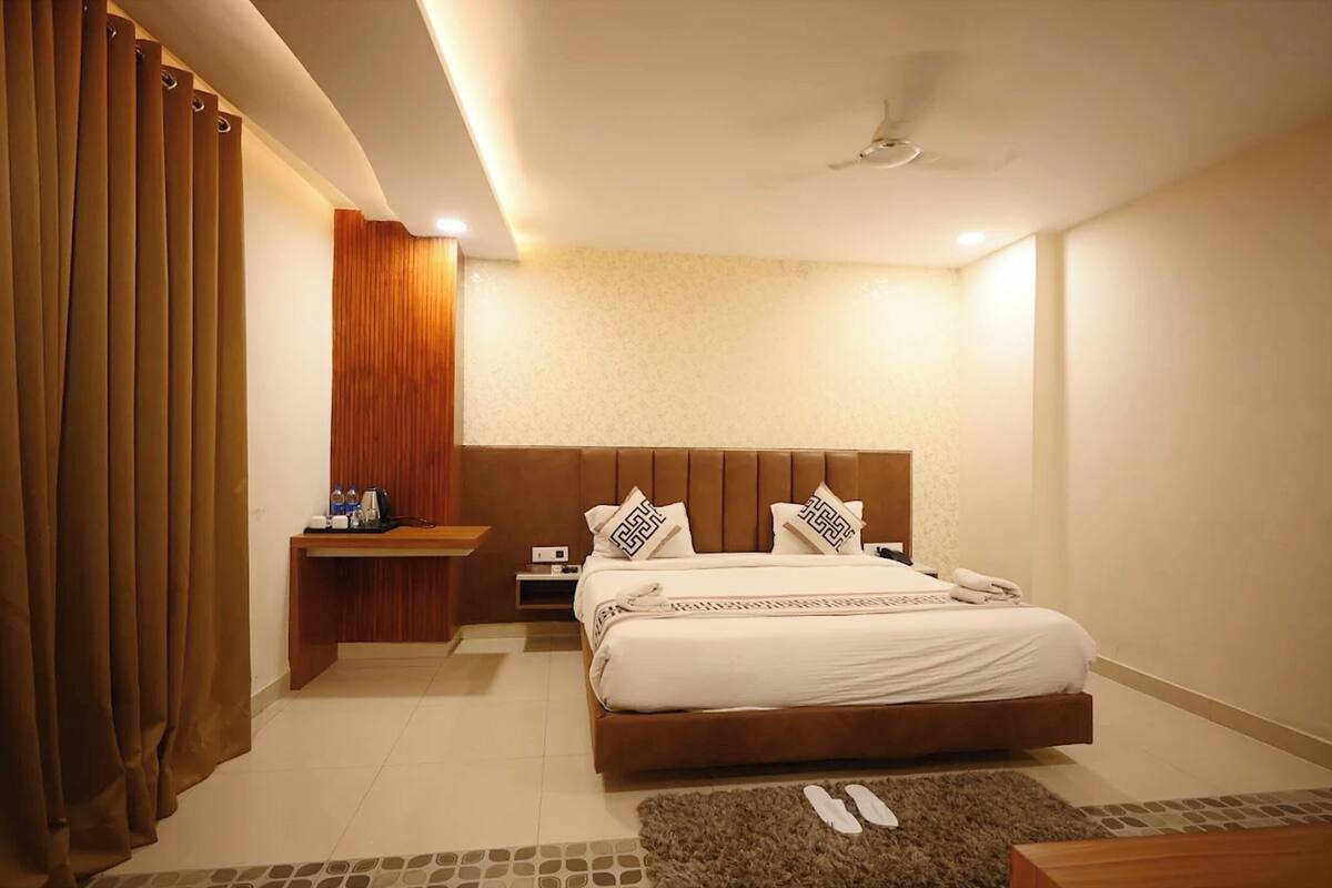 A modern hotel room with a large bed, wooden headboard, and a small bedside table with a lamp.