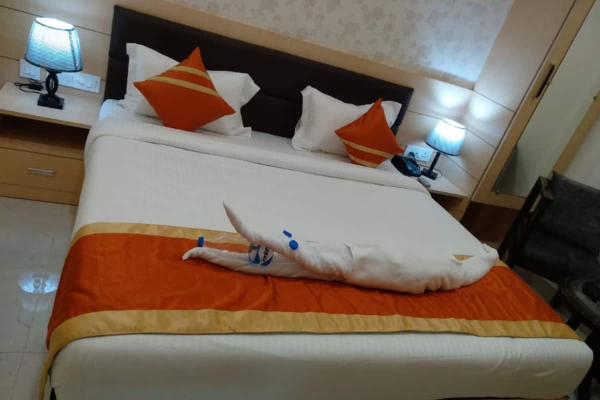A neatly made bed with an orange and white bedspread, two orange pillows, and a black headboard.