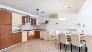 A compact kitchen with wooden cabinets, a built-in oven, a dishwasher, and a dining area with a table and chairs. - Villa Veruda by Villas Guide (Pula)