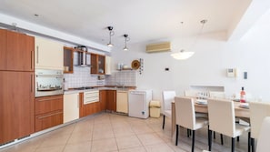 A compact kitchen with wooden cabinets, a built-in oven, a dishwasher, and a dining area with a table and chairs. - Villa Veruda by Villas Guide (Pula)
