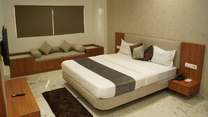 A modern bedroom with a large bed, a sofa bed, a wooden nightstand, and a TV. - Hotel Bajaj Residency (Nanded)