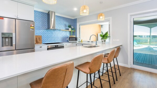 A modern kitchen with a large island, stainless steel appliances, and a view of a pool.