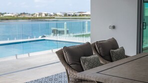 A balcony with a view of a swimming pool, a glass railing, and a table with chairs.