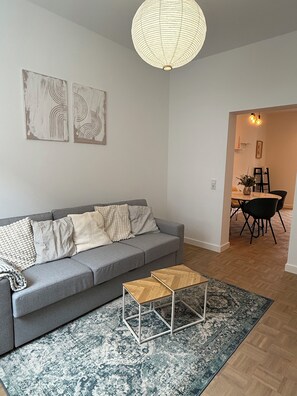 A modern living room with a grey sofa, a patterned rug, and a wooden coffee table. There are abstract wall art pieces and a hanging light fixture. - Cozy City Apartment - Quiet Area (Kaiserslautern)