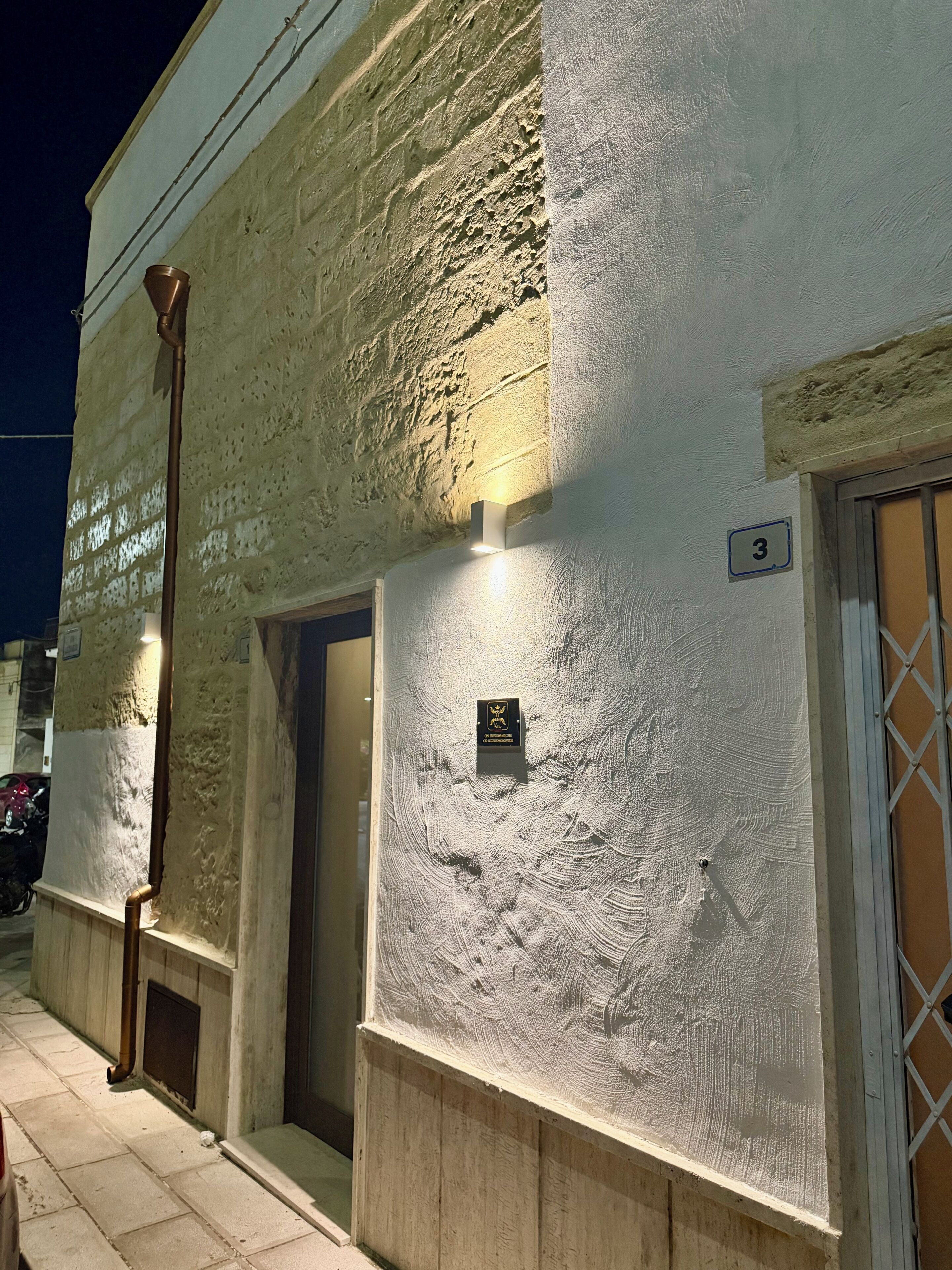 Um edifício com fachada texturizada, porta visível e placa com o número do apartamento.