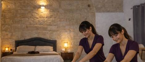 A massage therapy room with stone arches, a bed, and two massage therapists.