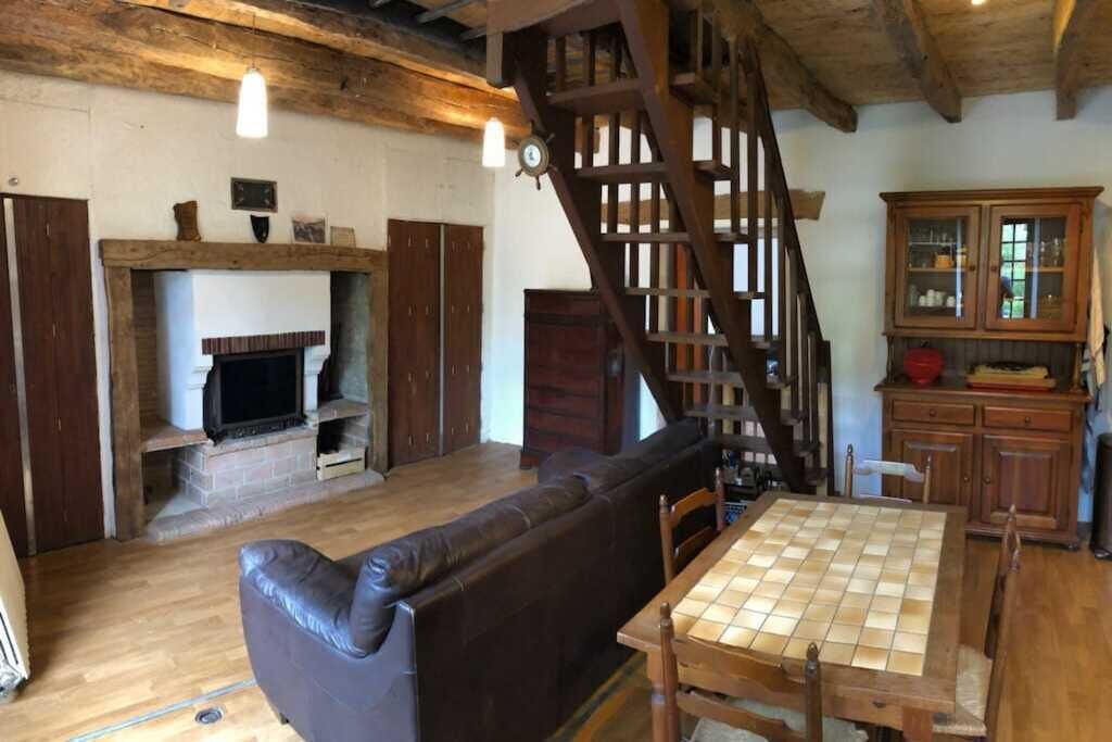Een rustiek interieur met een houten trap, een open haard, een leren bank en een eettafel.